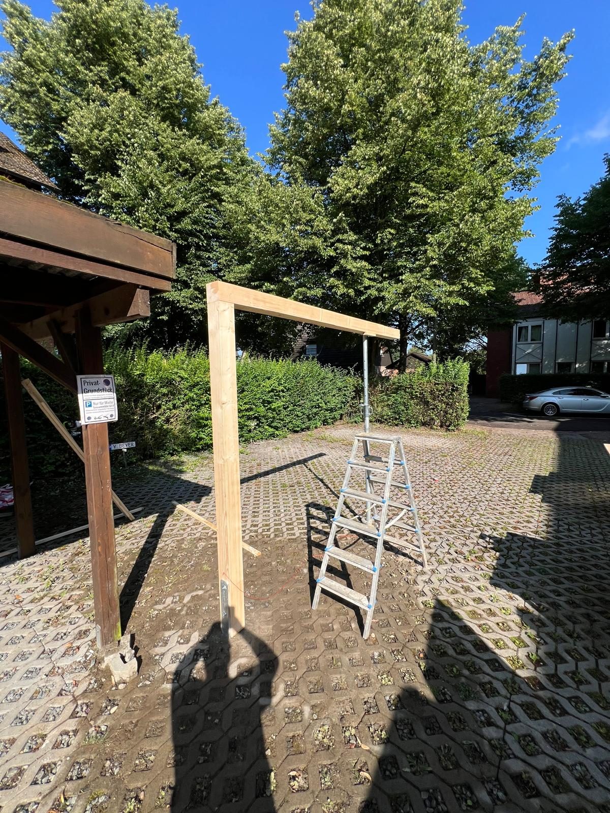 Beginn des Carport-Aufbaus: erste Holzpfosten stehen auf dem Pflasterstreifen