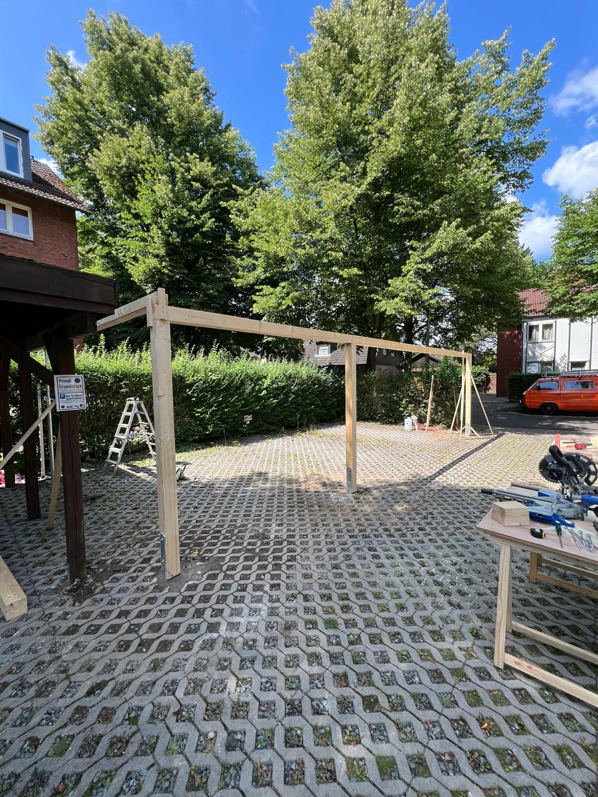 Carport-Konstruktion in der Bauphase mit Leiter und Werkzeug auf dem Pflaster
